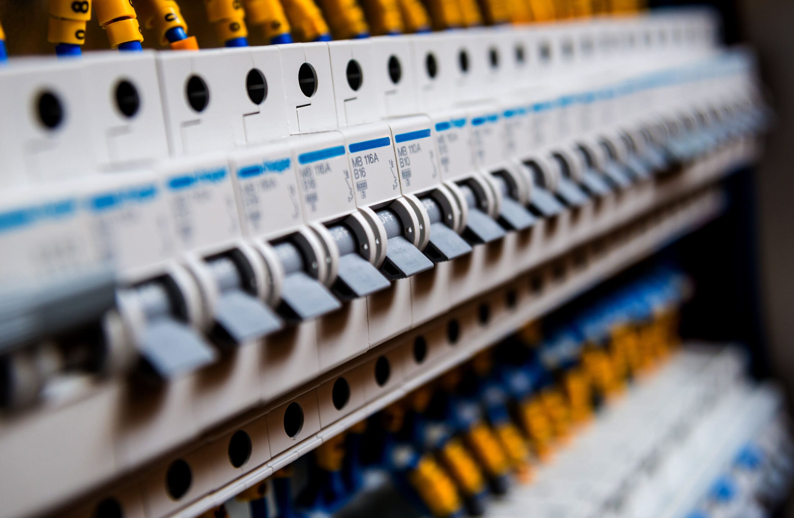 Close-up view of multiple electrical circuit breakers lined up in a row inside a panel, with yellow and blue wires visible above and below—ideal for an electrician inspecting solar panels or issuing landlord certificates.