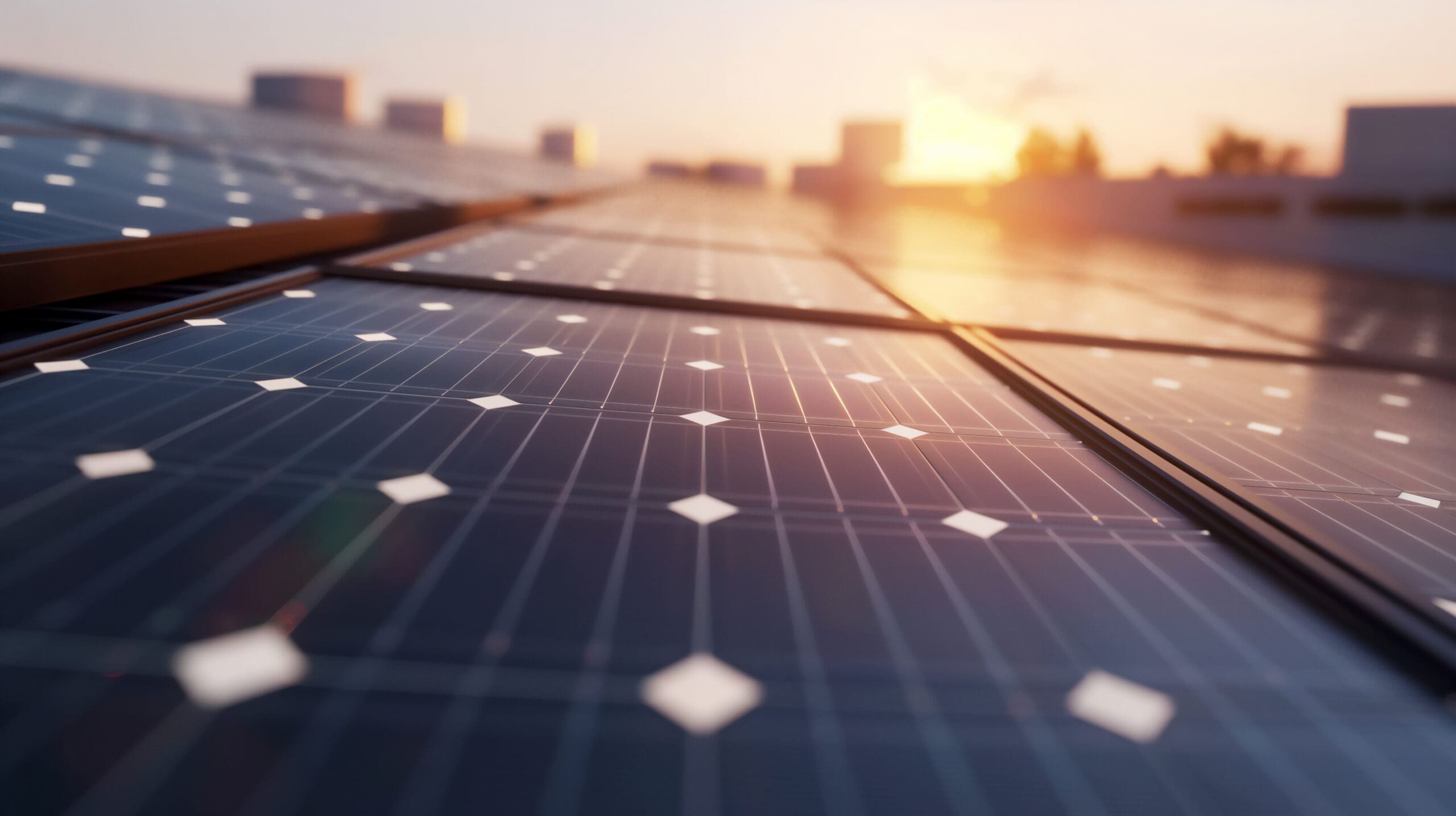 Close-up view of solar panels on a rooftop, part of modern electrical installations, with sunlight reflecting off their surface and a blurred cityscape in the background during sunrise or sunset.